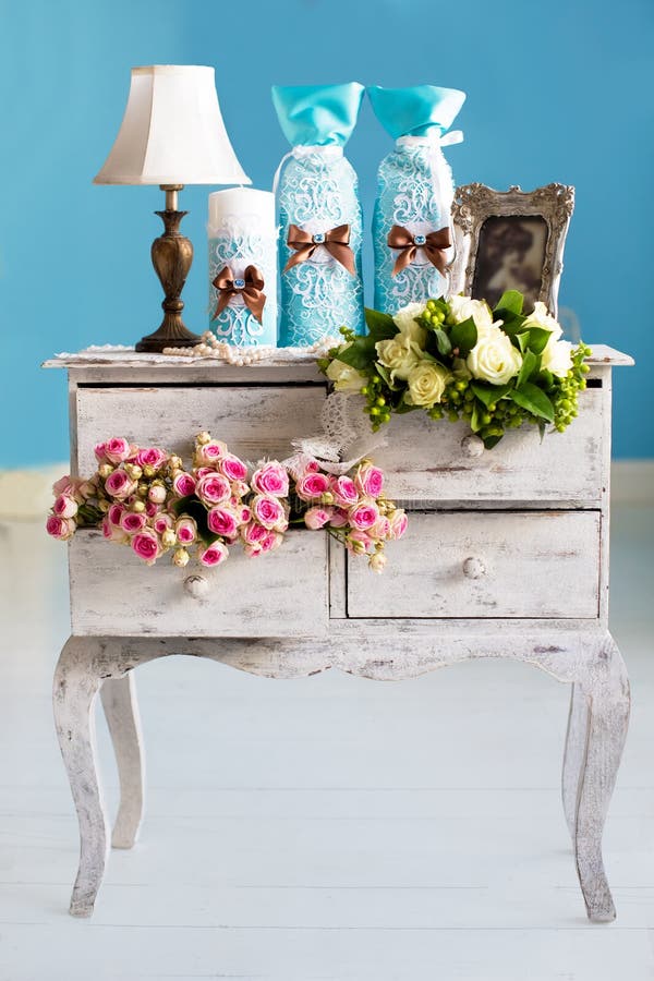 Wedding accessories for the morning, the bride in pink . Vintage commode with flowers. Candles, champagne, a string of pearls, rose.