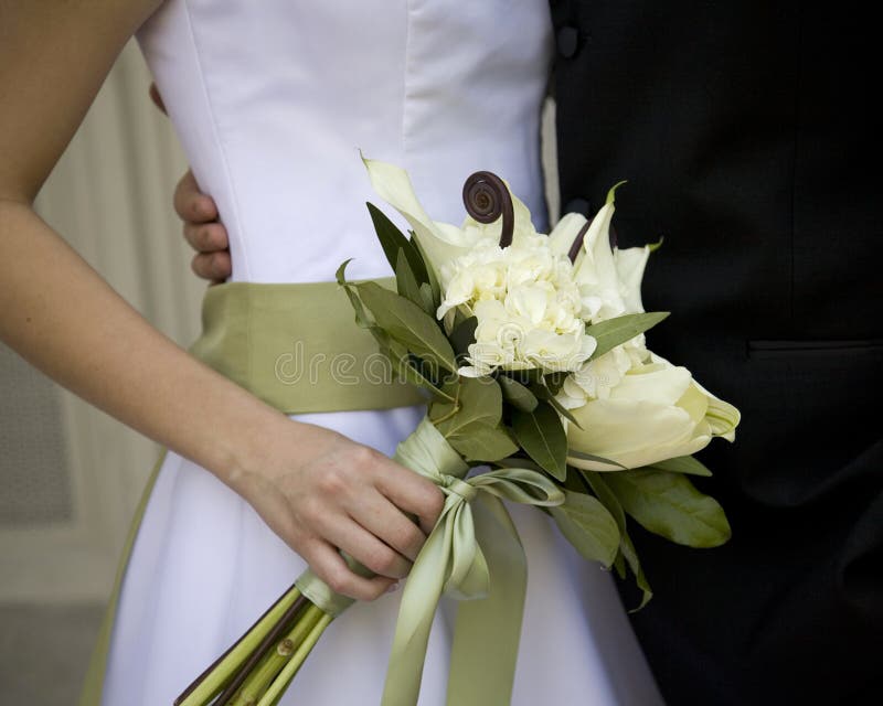 Close up of bride's hand holding bouquet made of white tulips, calla lilies and roses with stems wrapped in sage green ribbon. Close up of bride's hand holding bouquet made of white tulips, calla lilies and roses with stems wrapped in sage green ribbon