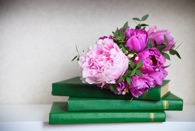 Wedding bouquet of a pink peonies, tulips and lily of the valley on the green books