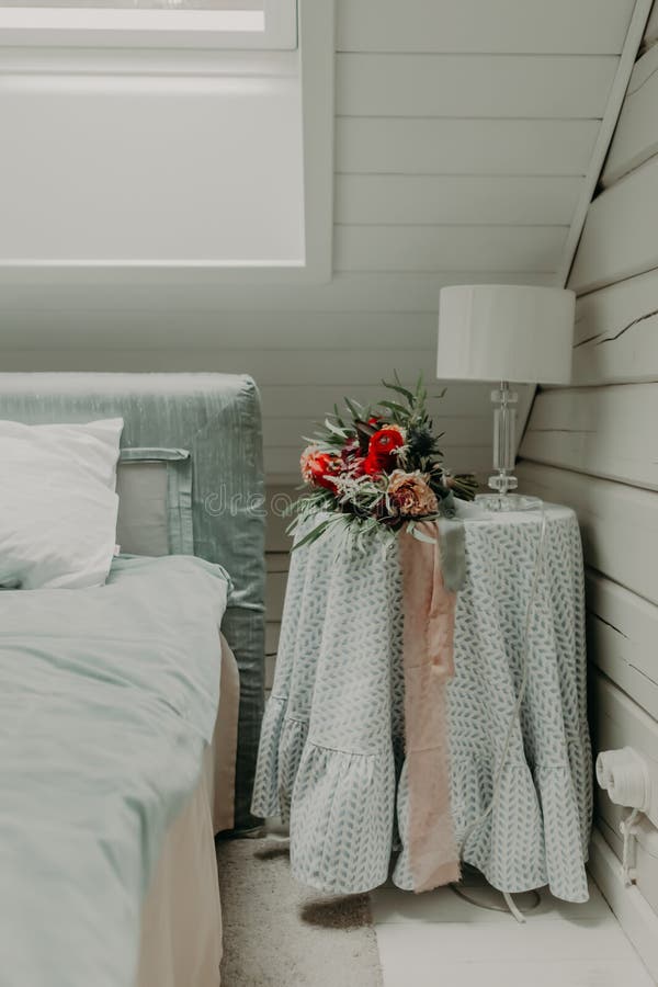 A wedding bouquet of red flowers decorated with a ribbon lies on the bedside table in the room.