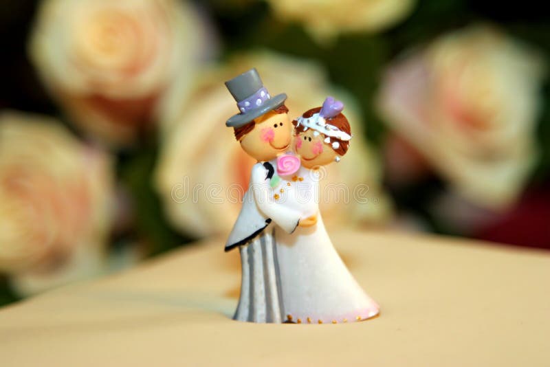Svatební dort panenky zblízka s růžemi na pozadí.