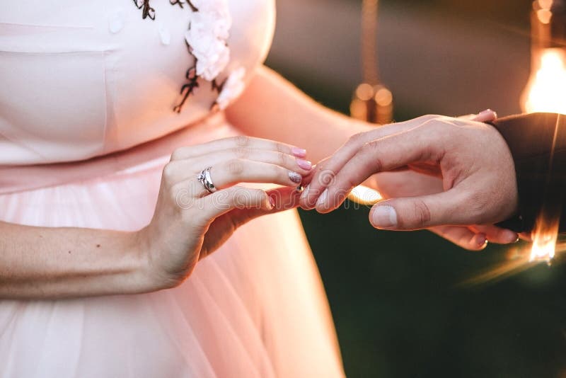 Wedding ceremony. The bride in a pink dress wears an engagement ring on a finger to the groom. On her hand is a gold ring with a d stock photo Wedding ceremony. The bride in a pink dress wears an engagement ring on a finger to the groom. On her hand is a gold ring with a d stock photo
