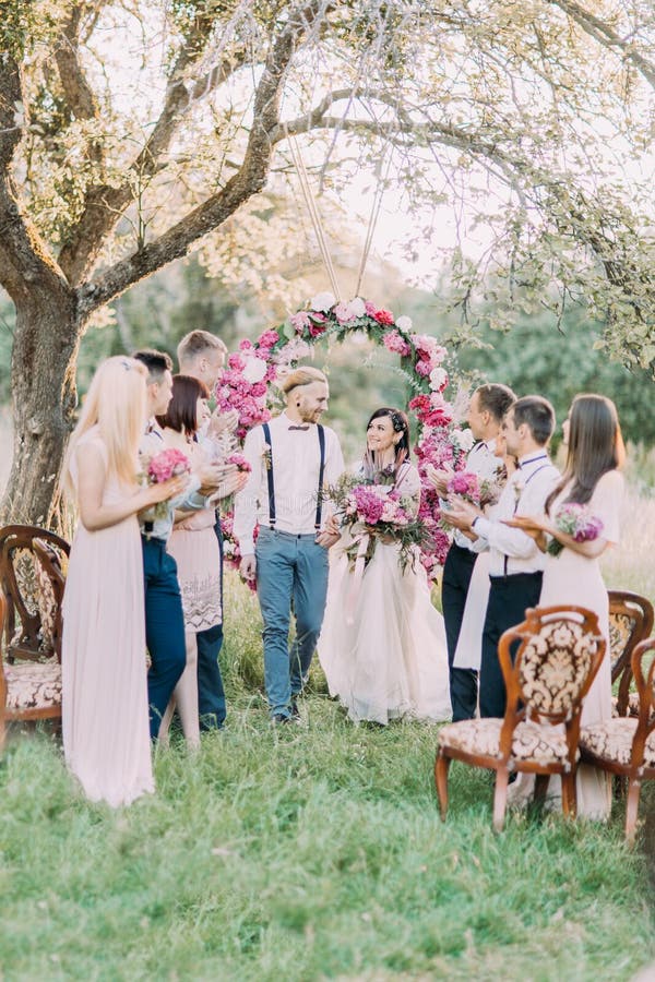 The wedding ceremony in the sunny park. The newlyweds are walking while their guests are applauding.