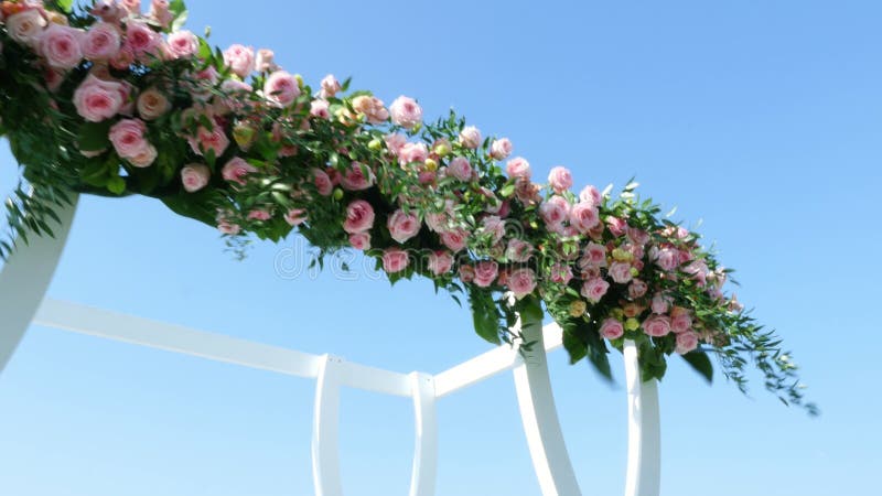 Wedding decor, white wedding arch decorated with roses, wedding ceremony on the beach, preparation for wedding ceremony