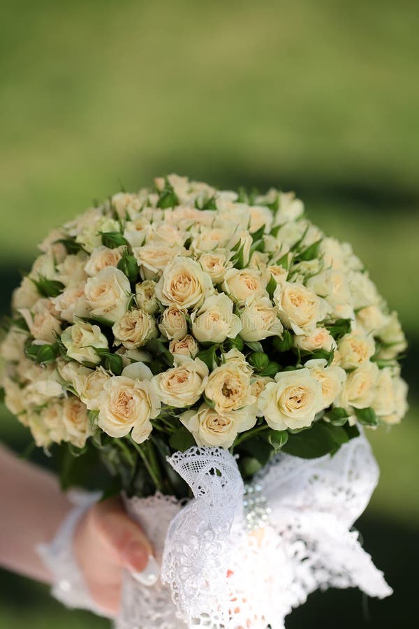Wedding flowers in hand. Closeup view of one beautiful fresh bright white yellow big wedding bouquet of rose flowers in hand of bride in white dress, vertical stock images Wedding flowers in hand. Closeup view of one beautiful fresh bright white yellow big wedding bouquet of rose flowers in hand of bride in white dress, vertical stock images