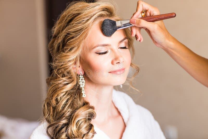 Wedding makeup artist making a make up for bride. Beautiful model girl indoors. Beauty blonde woman with curly hair