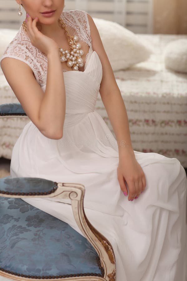 Wedding preparation. Beautiful young bride in white wedding dress indoors closeup. Luxury model sitting on vintage chair at home i royalty free stock photography Wedding preparation. Beautiful young bride in white wedding dress indoors closeup. Luxury model sitting on vintage chair at home i royalty free stock photography