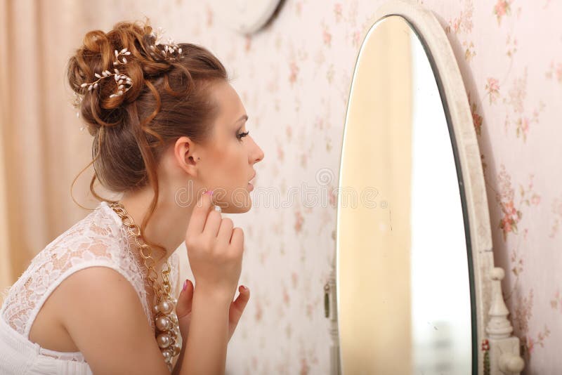 Wedding preparation. Beautiful young bride in white wedding dress indoors. Luxuty model looking at mirror and put on earring, at h royalty free stock photos Wedding preparation. Beautiful young bride in white wedding dress indoors. Luxuty model looking at mirror and put on earring, at h royalty free stock photos
