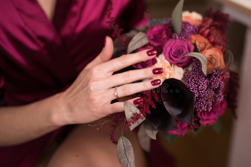 A wedding ring on the finger of the bride. Beautiful wedding bouquet in marsala colour in hands of the bride.
