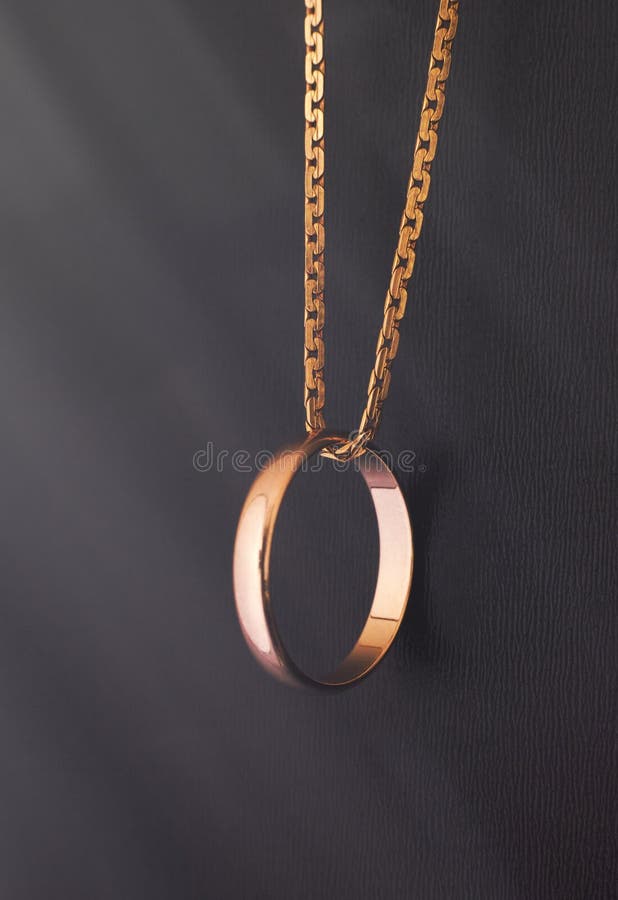 Gold Wedding Ring Hanging on Gold Chain on Black Background Stock Photo