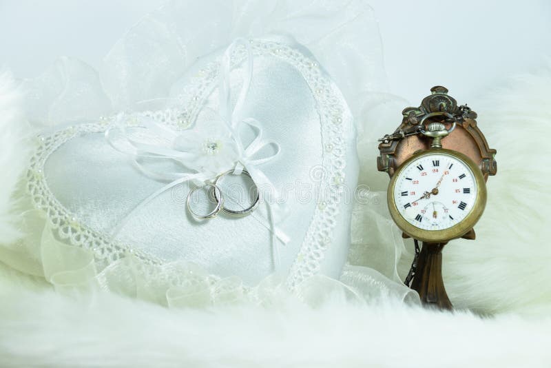 Wedding ring on heart pillow, clock on soft fabric