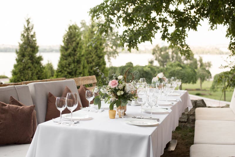 Wedding table setting decorated with fresh flowers in a brass vase. Wedding floristry. Banquet table for guests outdoors with a