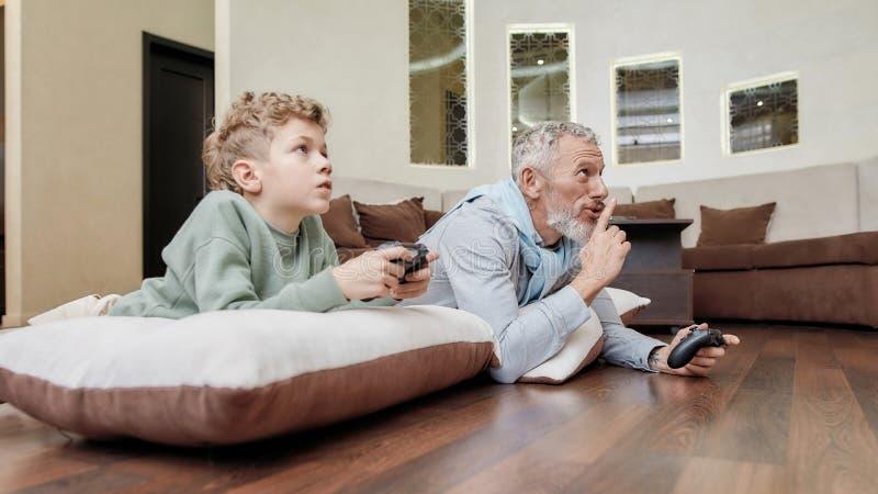 Weekend pigro con il nonno. nonno e il suo piccolo nipote carino che si stendono insieme per terra e giocano ai videogiochi fotografia stock