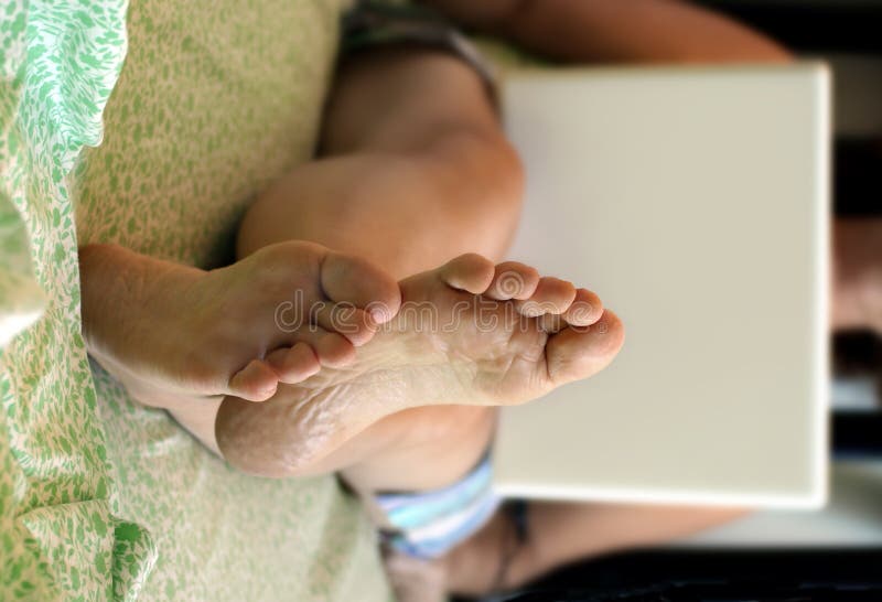 Una donna di lavorare su un computer portatile sul letto, piedi in primo piano, sfondo sfocato.