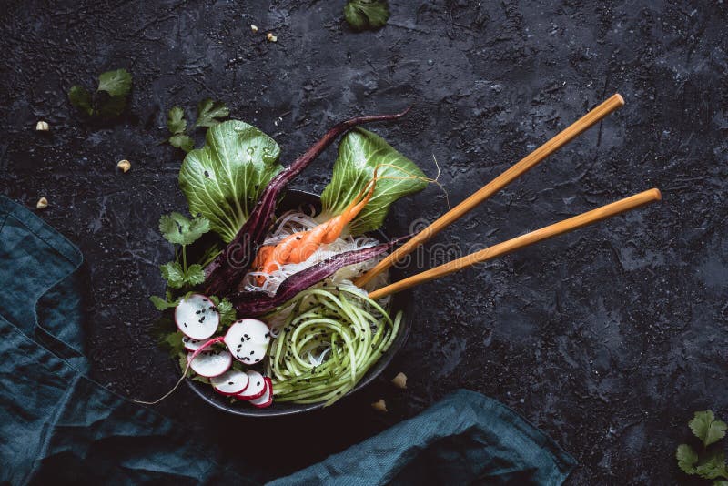 Weganinu puchar z chopsticks Azjatycka sałatka z ryżowymi kluskami, marchewką, rzodkwią i ogórkiem na czarnym tle, Odgórny widok fotografia stock