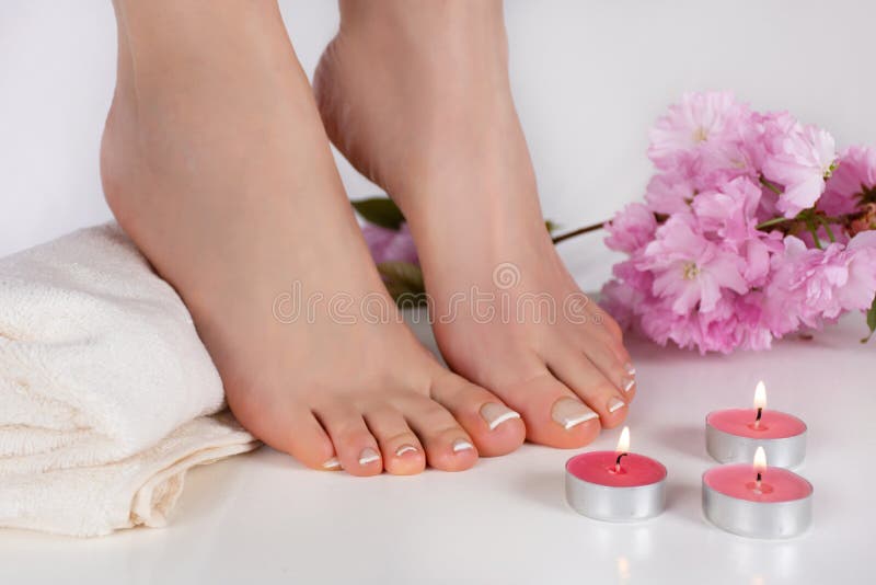 Weibliche bloße Füße mit französischem Nagellack auf weißem Tuch und dekorativen der Kerze, die auf Tabelle und rosa Blume brennt