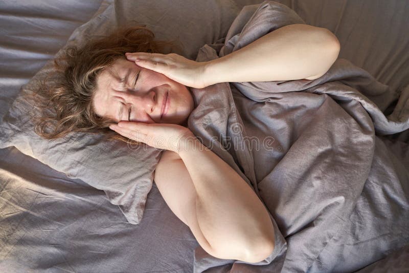 Weibliche erwachsene kaukasische Frau im Bett, die schmerzhaft am Kopf sitzt stockfoto