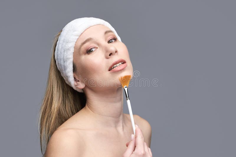 Weibliche erwachsene kaukasische Weibchen, die Make-up mit Pinsel mit weißem Kopfband anbringen stockfotografie
