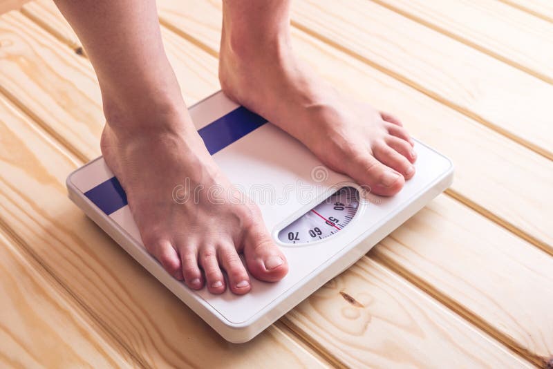 Female feet standing on mechanical scales for weight control on wooden background. The concept of slimming and weight loss. Female feet standing on mechanical scales for weight control on wooden background. The concept of slimming and weight loss