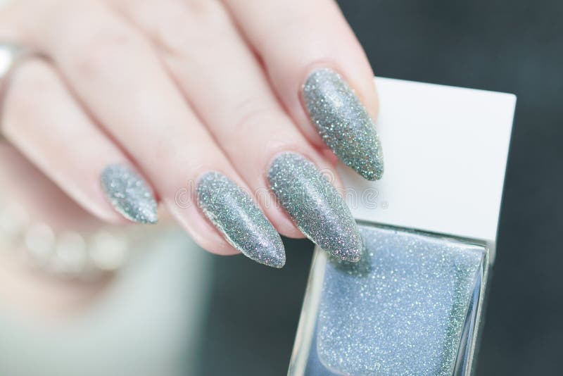 Weibliche Hand mit langen Nägeln und weißgraue silberne Maniküre lizenzfreie stockfotografie