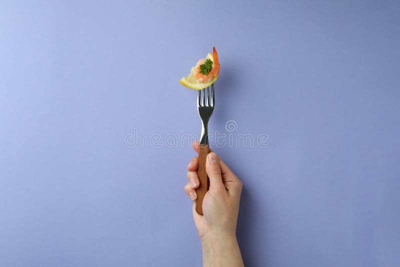 Weibliche Handgabel mit Garnelen und Zitrone auf violettem Hintergrund