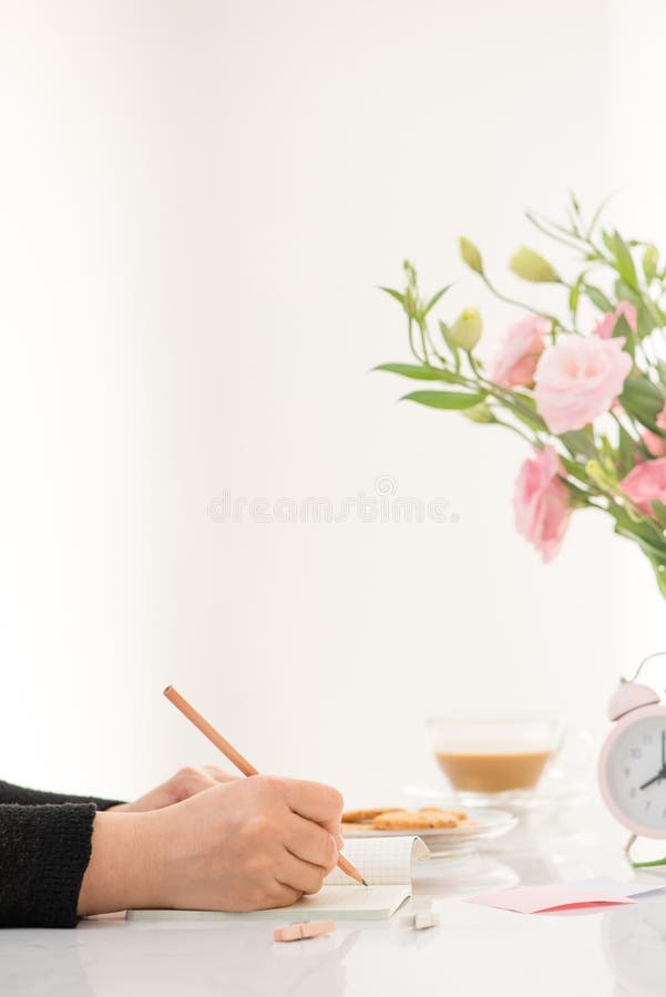 Weibliche Handschrift in einem Notizbuch am Schreibtisch, Draufsicht Auf den weißen Tabellenlageblumen