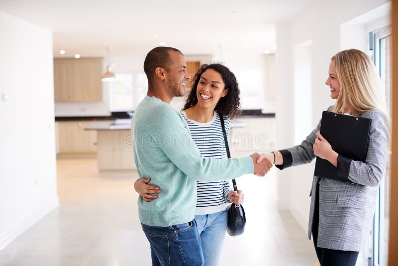 Female Realtor Shaking Hands With Couple Interested In Buying House. Female Realtor Shaking Hands With Couple Interested In Buying House