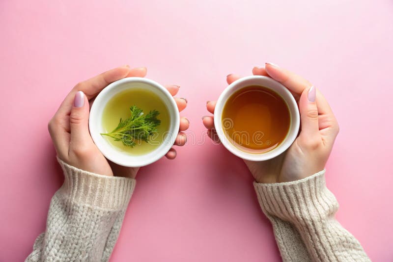 Weibliche Hände mit einer Tasse schwarzen Tees und einer Tasse grünen Tees auf rosa Hintergrund lizenzfreie abbildung
