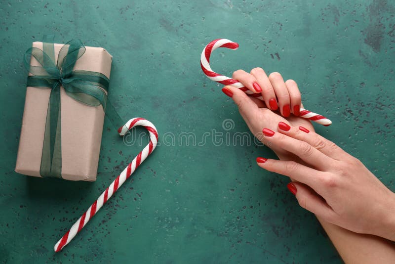 Weibliche Hände mit Zuckerstangen und Geschenkbox auf grünem Hintergrund lizenzfreie stockbilder Weibliche Hände mit Zuckerstangen und Geschenkbox auf grünem Hintergrund lizenzfreie stockbilder