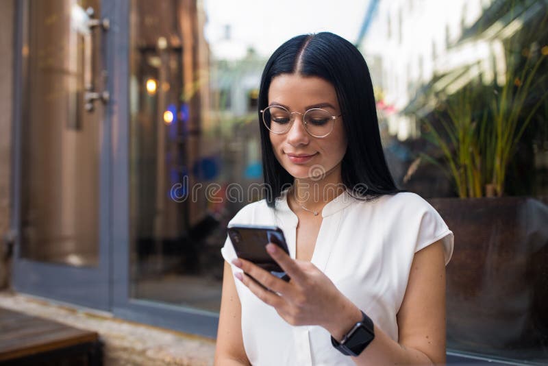 Weibliche on-line-Anmeldung über Smartphone, während in der Kaffeestube Nähe Fenster nach draußen sein lizenzfreies stockbild