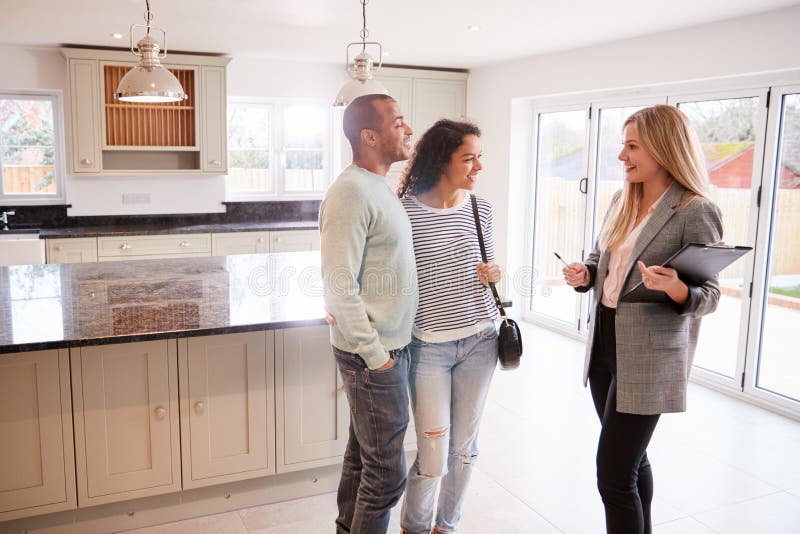 Female Realtor Showing Couple Interested In Buying Around House. Female Realtor Showing Couple Interested In Buying Around House