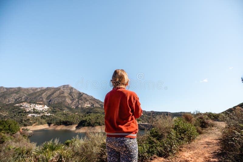 Weiblicher kaukasischer Erwachsener genießt einen malerischen Bergblick nahe Stausee unter freiem Himmel stockbild