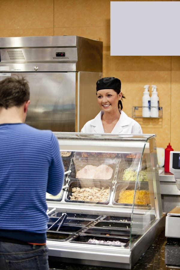 Female cook waiting for a student to choose his lunch in the cafeteria. Female cook waiting for a student to choose his lunch in the cafeteria