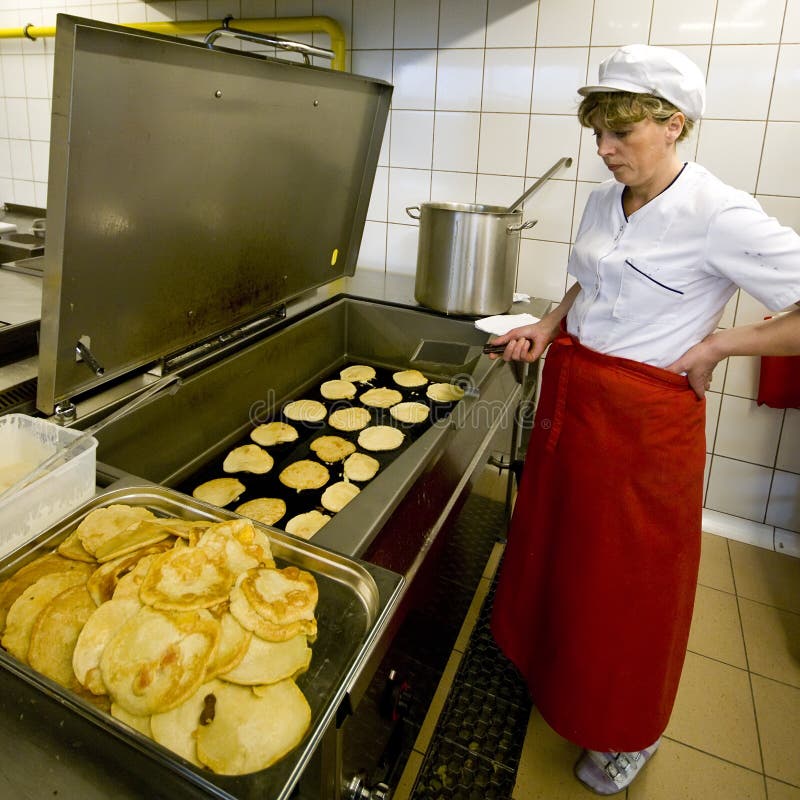 A female cook working in an industrial kitchen, standing at a large frying pan, making pancakes. A female cook working in an industrial kitchen, standing at a large frying pan, making pancakes.