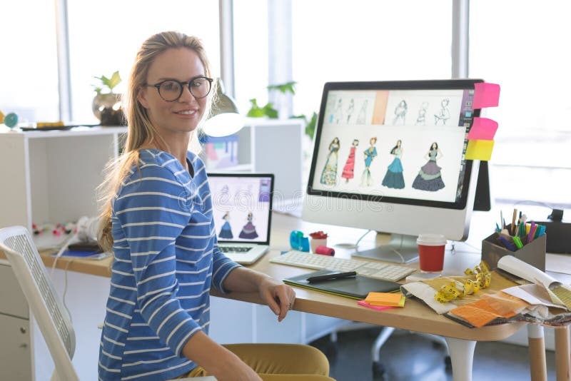 Weiblicher Modedesigner, der Kamera beim Sitzen am Schreibtisch in einem modernen Büro betrachtet lizenzfreie stockfotos Weiblicher Modedesigner, der Kamera beim Sitzen am Schreibtisch in einem modernen Büro betrachtet lizenzfreie stockfotos