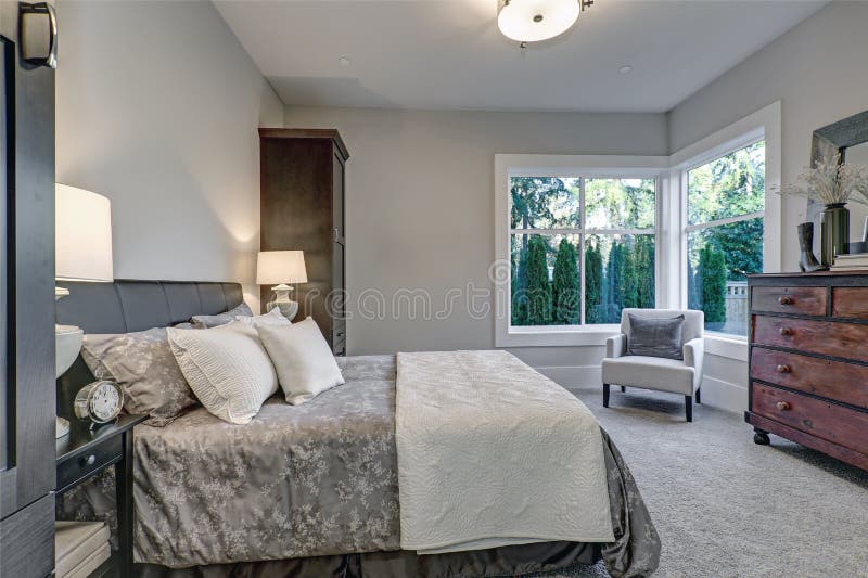 Cozy bedroom interior features soft gray walls framing queen bed dressed in grey and blue bedding and flanked by tall dark brown cabinets. Northwest, USA. Cozy bedroom interior features soft gray walls framing queen bed dressed in grey and blue bedding and flanked by tall dark brown cabinets. Northwest, USA