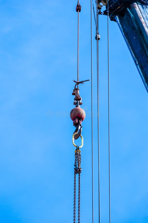 Weight with hook and chains near cables hanging down from top of industrial crane against blue sky. Weight with hook and chains near cables hanging down from top of industrial crane against blue sky.