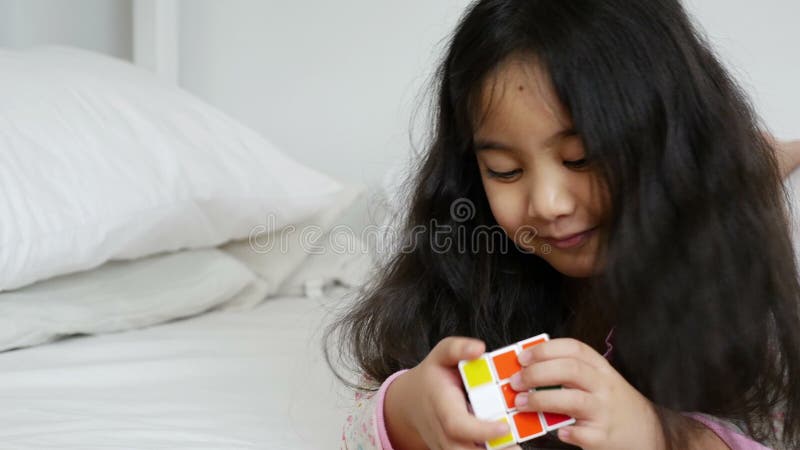 Weinig Aziatisch meisje die rubik kubeert op het bed spelen