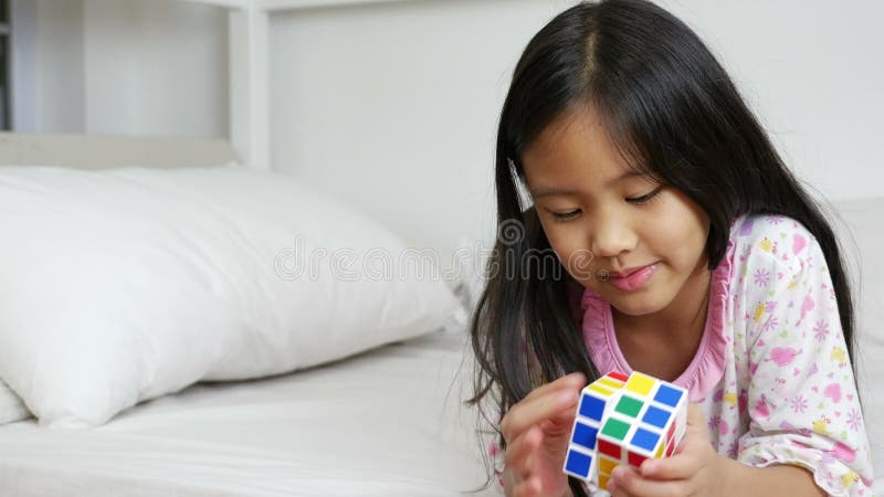 Weinig Aziatisch meisje die rubik kubeert op het bed spelen