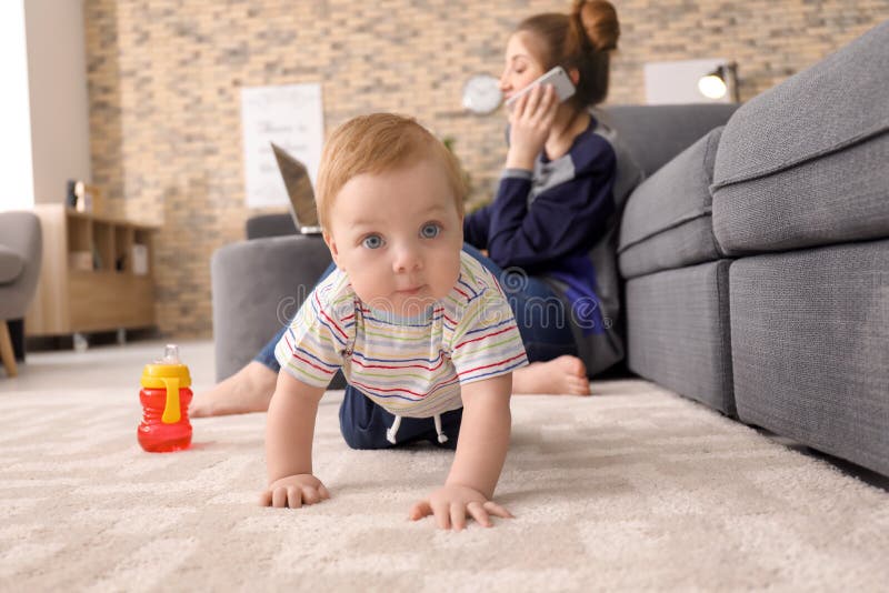 Weinig baby die op tapijt kruipen terwijl moeder die thuis werken royalty-vrije stock foto's Weinig baby die op tapijt kruipen terwijl moeder die thuis werken royalty-vrije stock foto's