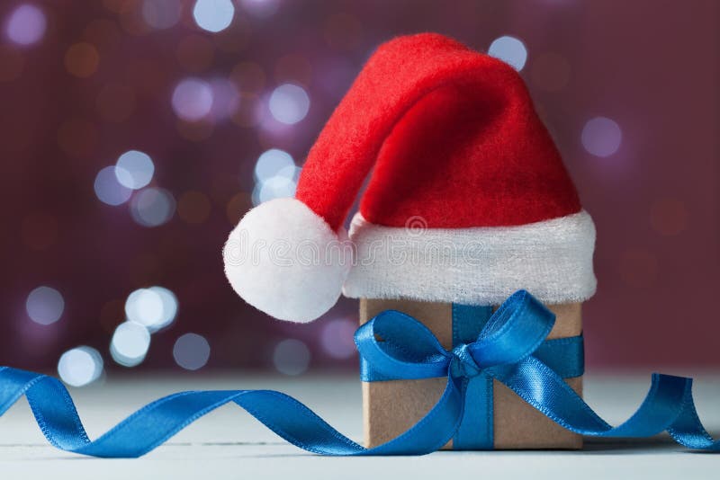 Little christmas gift box or present and santa hat against bokeh background. Holiday greeting card. Little christmas gift box or present and santa hat against bokeh background. Holiday greeting card.