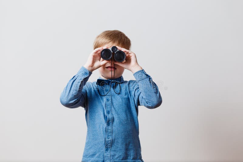 Weinig jongen in het blauwe overhemd kijkt door verrekijkers royalty-vrije stock fotografie Weinig jongen in het blauwe overhemd kijkt door verrekijkers royalty-vrije stock fotografie
