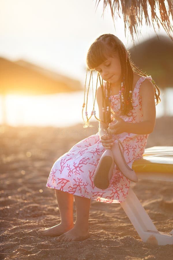 Weinig mooie meisjeszitting op het strand bij zonsondergang royalty-vrije stock fotografie Weinig mooie meisjeszitting op het strand bij zonsondergang royalty-vrije stock fotografie