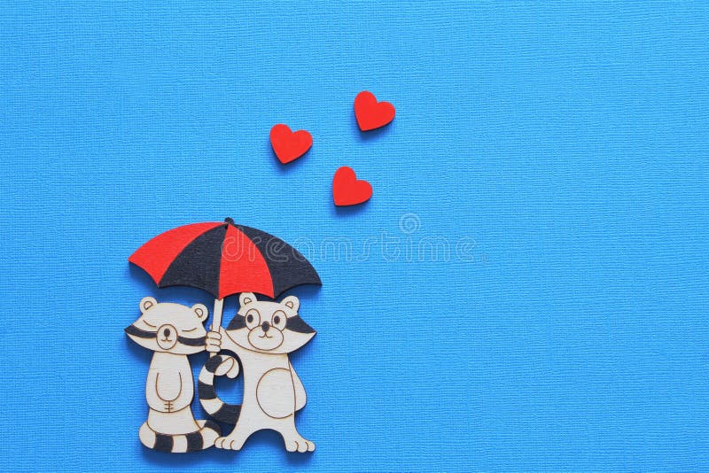 Weinlese, die stilisierte Figürchen von Liebhaberwaschbären unter Regenschirm mit roten Herzen auf hellem blauem Hintergrund beza lizenzfreies stockfoto Weinlese, die stilisierte Figürchen von Liebhaberwaschbären unter Regenschirm mit roten Herzen auf hellem blauem Hintergrund beza lizenzfreies stockfoto