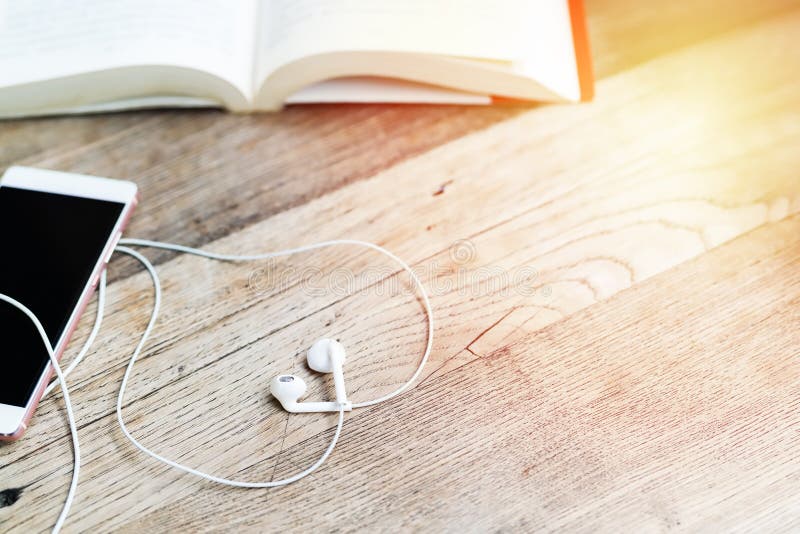 Weißer Herzformkopfhörer mit Smartphone und offenem Buch auf Arbeitstischplatteansicht mit Kopienraum stockfotografie Weißer Herzformkopfhörer mit Smartphone und offenem Buch auf Arbeitstischplatteansicht mit Kopienraum stockfotografie
