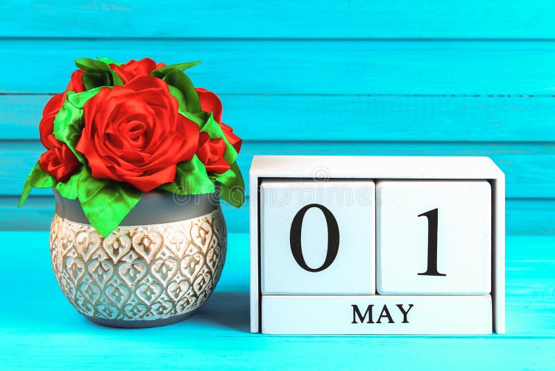 White wooden calendar with the text: May 1. DIY rose on a blue wooden table. Labor Day and Spring. White wooden calendar with the text: May 1. DIY rose on a blue wooden table. Labor Day and Spring