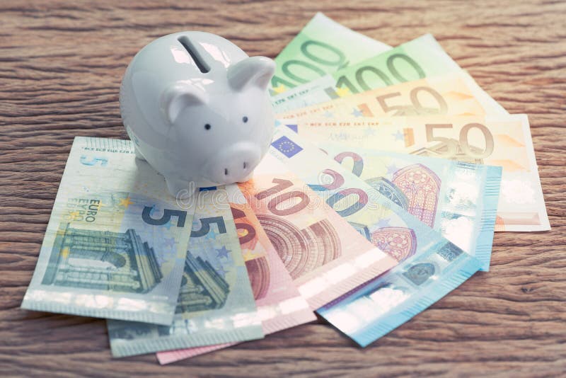Weißes Sparschwein auf Stapel von Eurobanknoten auf Holztisch, fina stockbild Weißes Sparschwein auf Stapel von Eurobanknoten auf Holztisch, fina stockbild