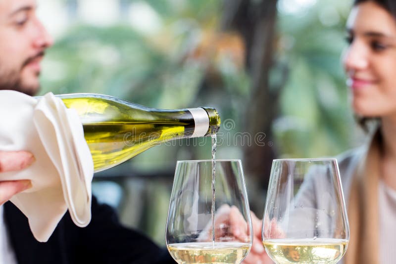 Weißwein, das mit Paaren im Hintergrund gießt stockfotografie Weißwein, das mit Paaren im Hintergrund gießt stockfotografie
