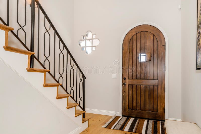 White-walled entryway with wooden door and black iron railing. White-walled entryway with wooden door and black iron railing