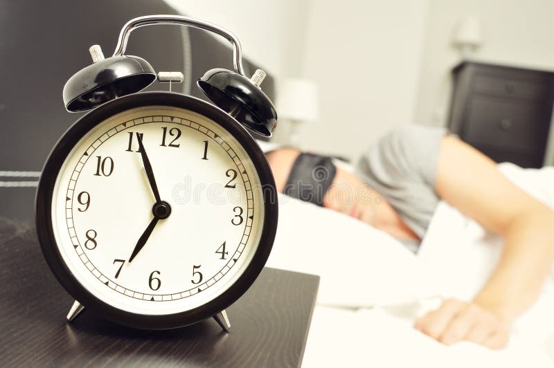 Wekker en jonge mensenslaap in bed met een slaapmasker stock afbeeldingen Wekker en jonge mensenslaap in bed met een slaapmasker stock afbeeldingen